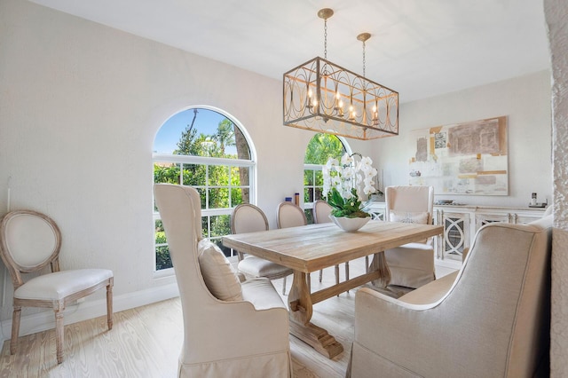 dining space with baseboards, a notable chandelier, and light wood finished floors