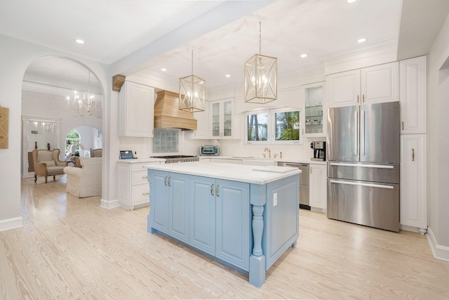 kitchen with arched walkways, stainless steel appliances, light countertops, a center island, and glass insert cabinets