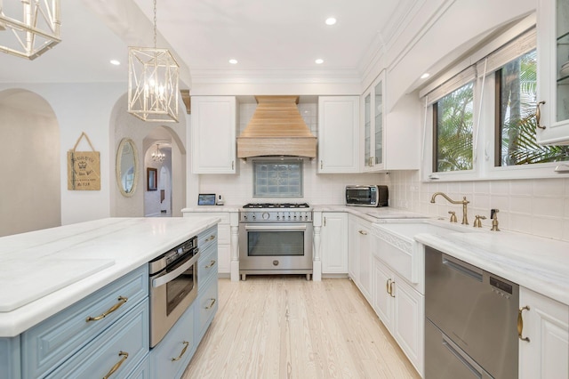 kitchen with stainless steel appliances, a sink, white cabinets, glass insert cabinets, and custom range hood