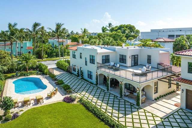 rear view of property featuring a patio, a balcony, an outdoor pool, a lawn, and stucco siding