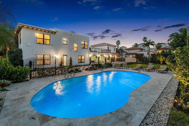 pool at dusk with a patio area, a gate, fence, and a fenced in pool