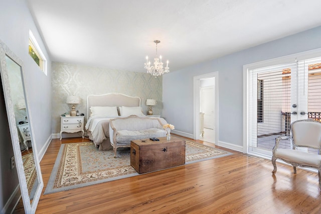 bedroom with a notable chandelier, an accent wall, wood finished floors, access to outside, and baseboards