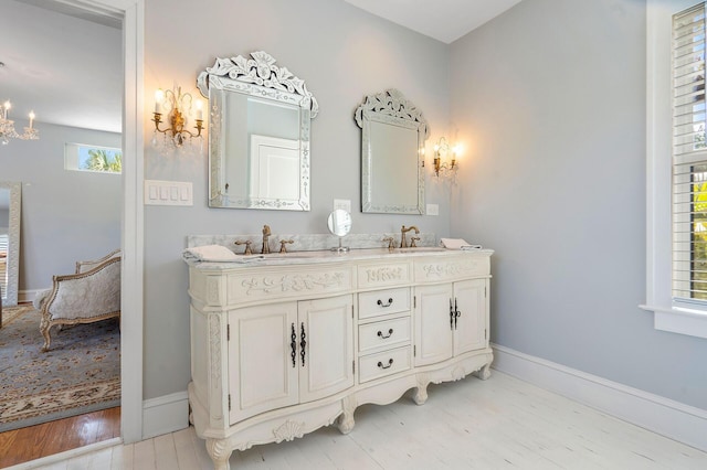 ensuite bathroom with double vanity, baseboards, a sink, and wood finished floors