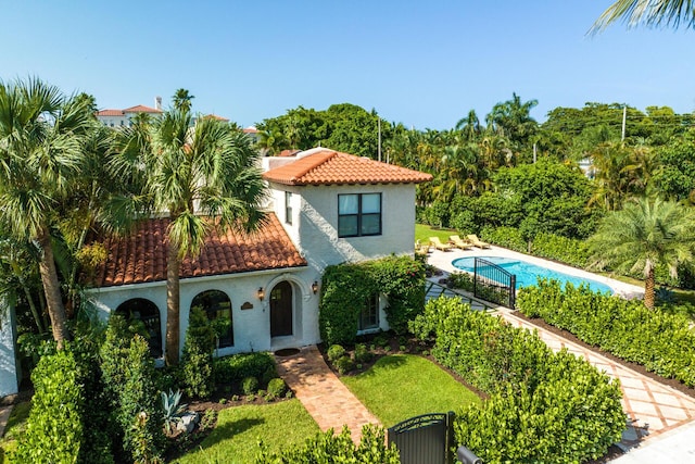 mediterranean / spanish house with a tile roof, a front lawn, an outdoor pool, and stucco siding