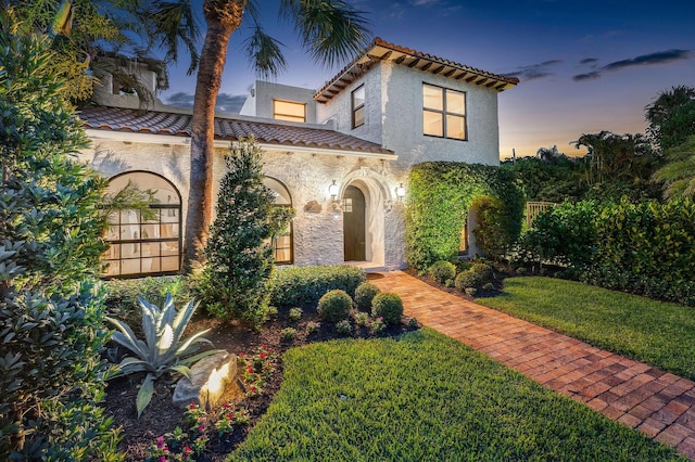 mediterranean / spanish-style home featuring a front yard, a tile roof, and stucco siding