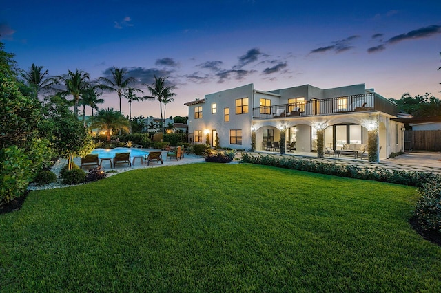 rear view of property featuring a balcony, stucco siding, a yard, and a patio