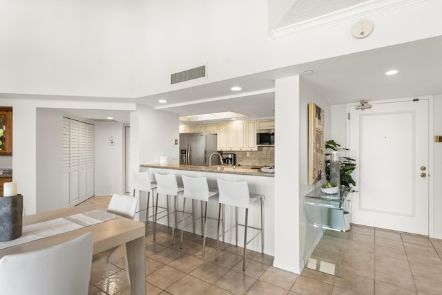 kitchen with a kitchen breakfast bar, backsplash, appliances with stainless steel finishes, light tile patterned floors, and ornamental molding