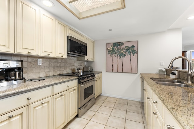 kitchen featuring light stone countertops, sink, cream cabinets, light tile patterned floors, and appliances with stainless steel finishes