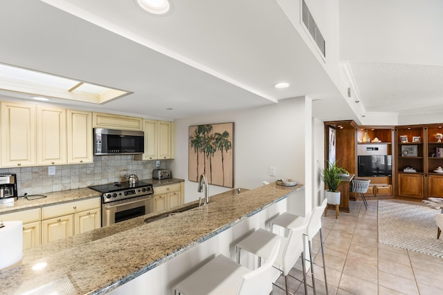 kitchen with light stone countertops, sink, a breakfast bar, light tile patterned floors, and appliances with stainless steel finishes