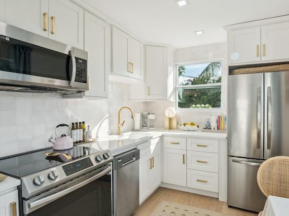 kitchen featuring sink, white cabinets, backsplash, light hardwood / wood-style floors, and stainless steel appliances