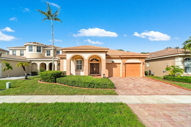 mediterranean / spanish home featuring a tiled roof, a front yard, stucco siding, decorative driveway, and an attached garage