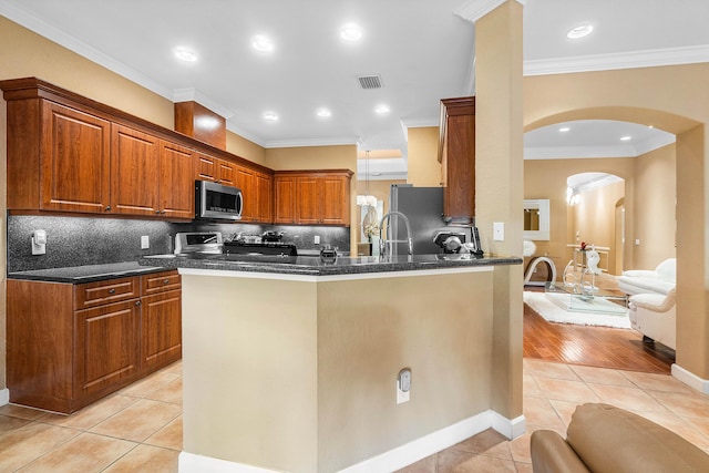 kitchen with kitchen peninsula, backsplash, stainless steel appliances, crown molding, and light tile patterned floors