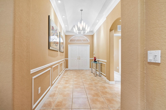 hallway with a notable chandelier, arched walkways, light tile patterned flooring, crown molding, and a decorative wall