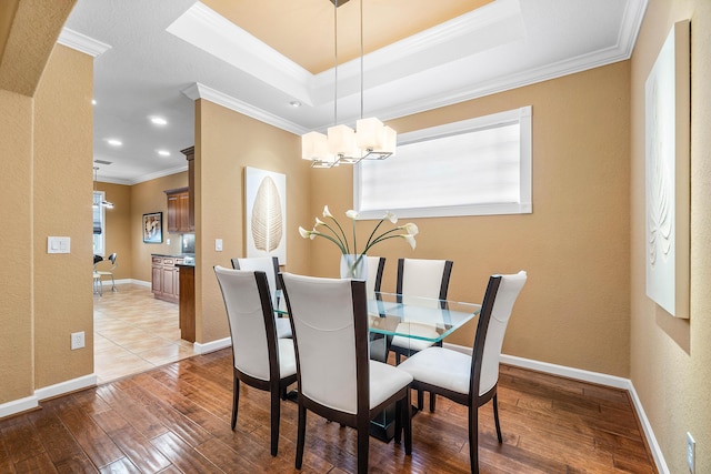 dining room featuring a chandelier, light wood-type flooring, a tray ceiling, and crown molding