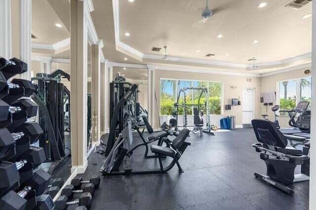 gym featuring a tray ceiling, ceiling fan, and ornamental molding