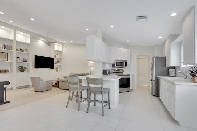 kitchen featuring appliances with stainless steel finishes, a kitchen breakfast bar, light tile patterned floors, built in features, and white cabinetry