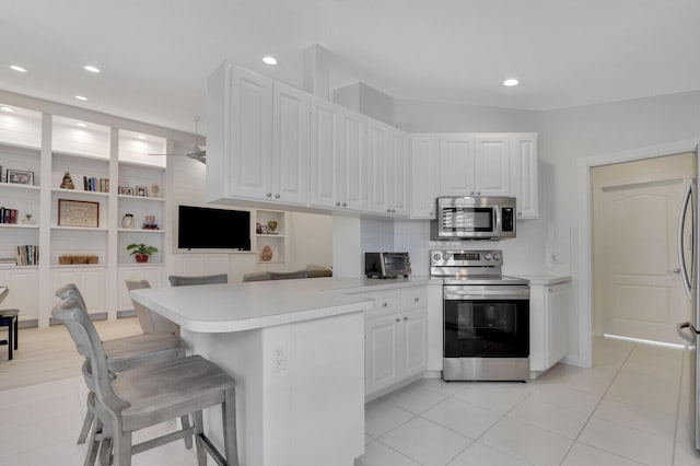 kitchen with stainless steel appliances, white cabinets, kitchen peninsula, a breakfast bar, and light tile patterned flooring