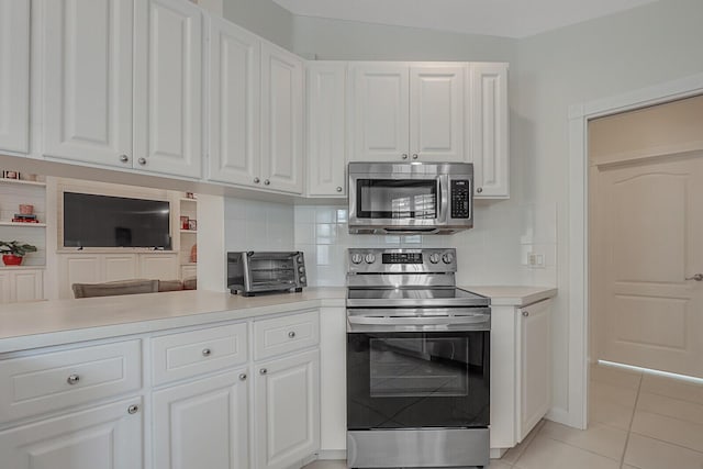 kitchen with appliances with stainless steel finishes, light tile patterned floors, tasteful backsplash, and white cabinetry