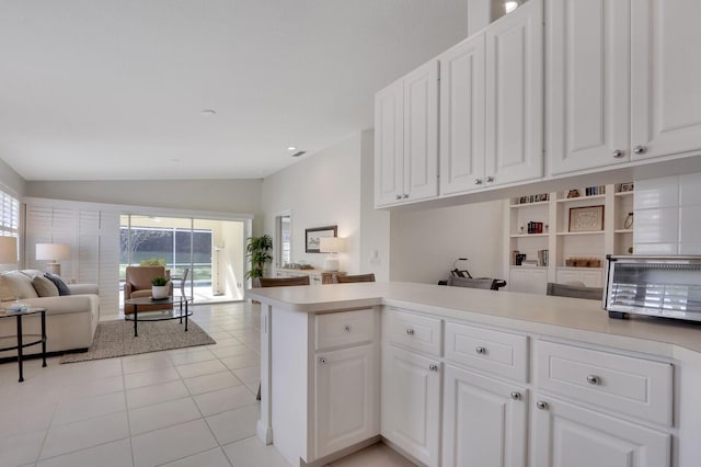 kitchen with kitchen peninsula, white cabinets, light tile patterned flooring, and vaulted ceiling