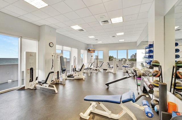 exercise room featuring a drop ceiling, a water view, and a healthy amount of sunlight