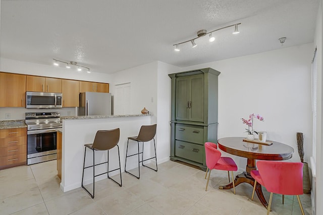 kitchen with light stone countertops, light tile patterned floors, a textured ceiling, and appliances with stainless steel finishes