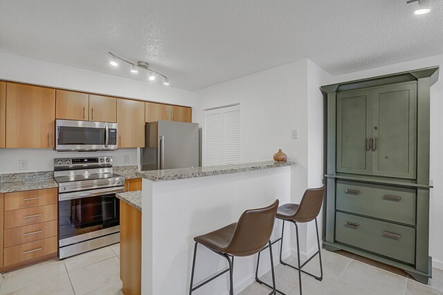 kitchen with a textured ceiling, light tile patterned flooring, light stone countertops, and stainless steel appliances