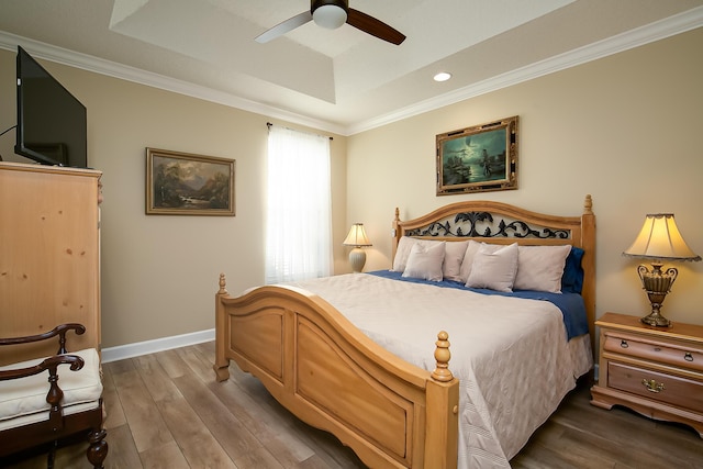 bedroom featuring hardwood / wood-style floors, ceiling fan, ornamental molding, and a tray ceiling