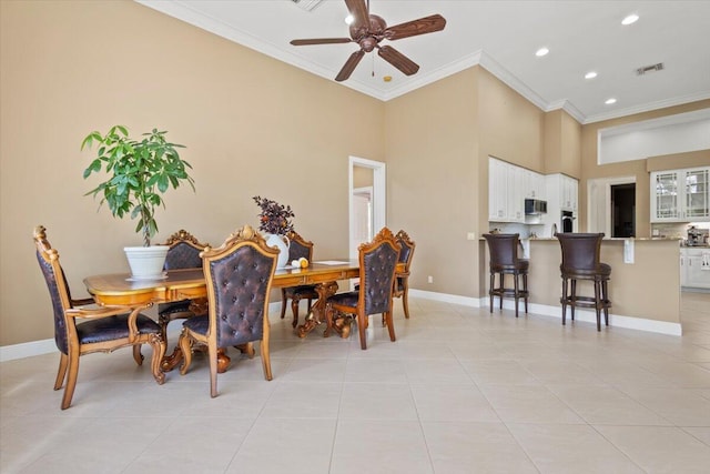 tiled dining space with ceiling fan, ornamental molding, and a high ceiling