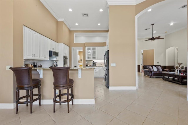 kitchen featuring white cabinets, ceiling fan, a kitchen bar, and light stone countertops