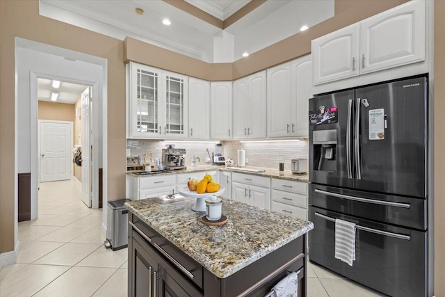 kitchen featuring light tile patterned flooring, white cabinets, stainless steel fridge, a kitchen island, and light stone counters