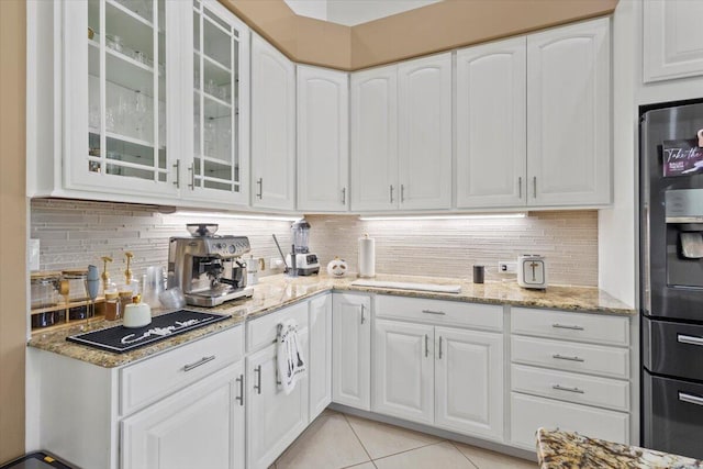 kitchen with white cabinets, backsplash, light stone counters, and light tile patterned flooring