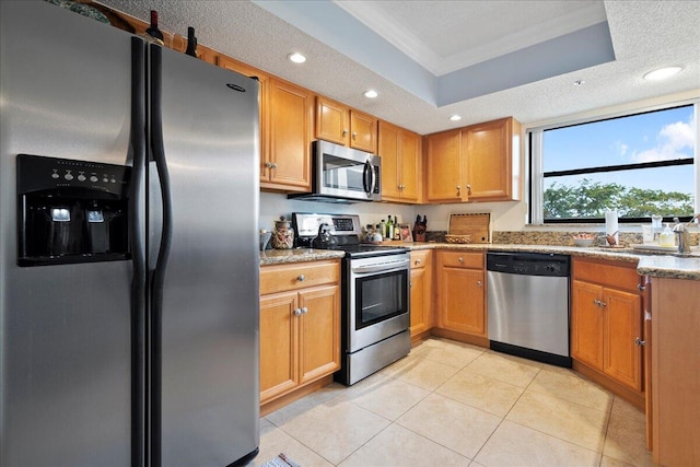 kitchen featuring light stone counters, a tray ceiling, stainless steel appliances, and a textured ceiling