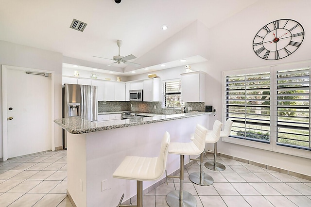 kitchen with kitchen peninsula, white cabinets, stainless steel appliances, and vaulted ceiling