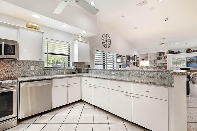 kitchen featuring lofted ceiling, kitchen peninsula, appliances with stainless steel finishes, tasteful backsplash, and white cabinetry