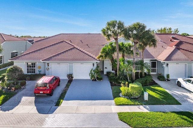 mediterranean / spanish-style home with a tiled roof, decorative driveway, an attached garage, and stucco siding