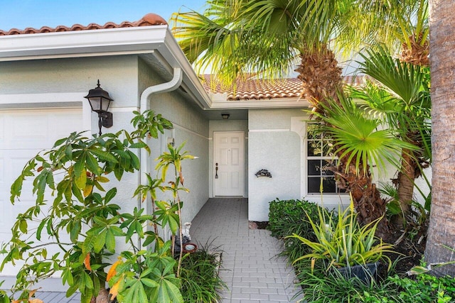 property entrance featuring an attached garage, a tile roof, and stucco siding