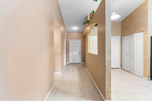 corridor with light tile patterned flooring, a textured ceiling, and baseboards