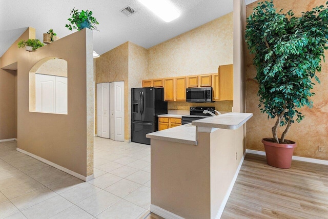 kitchen with visible vents, a peninsula, light countertops, black appliances, and high vaulted ceiling