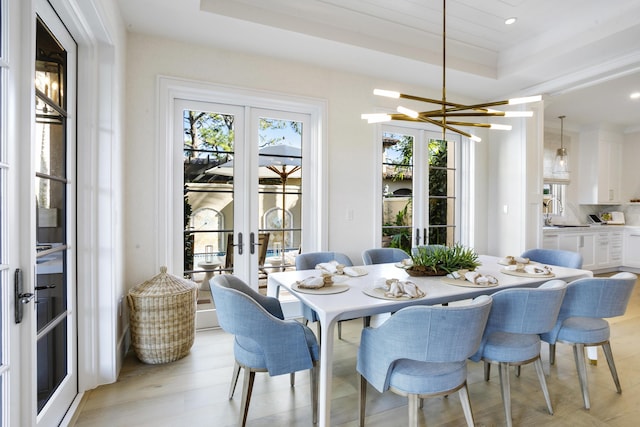 dining room featuring sink, french doors, a raised ceiling, light hardwood / wood-style flooring, and a notable chandelier