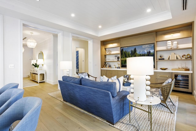 living room with built in shelves, light wood-type flooring, beverage cooler, and a tray ceiling