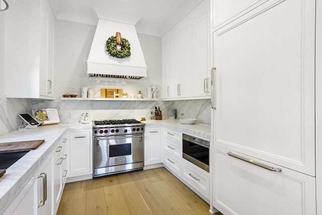 kitchen with tasteful backsplash, custom range hood, designer stove, light hardwood / wood-style floors, and white cabinetry