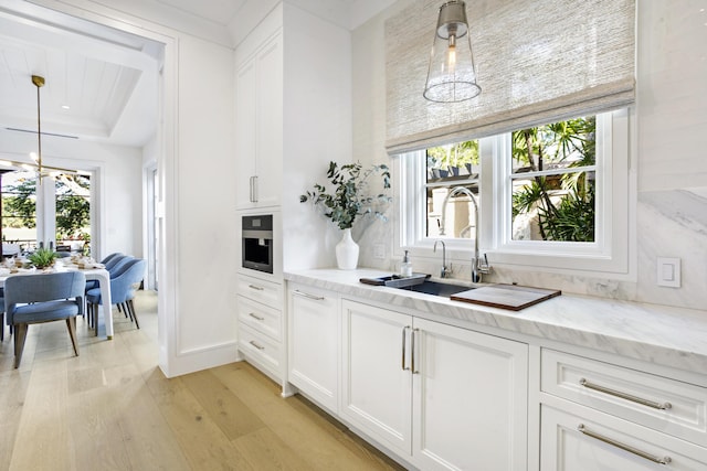 kitchen with decorative light fixtures, white cabinetry, sink, and light hardwood / wood-style flooring