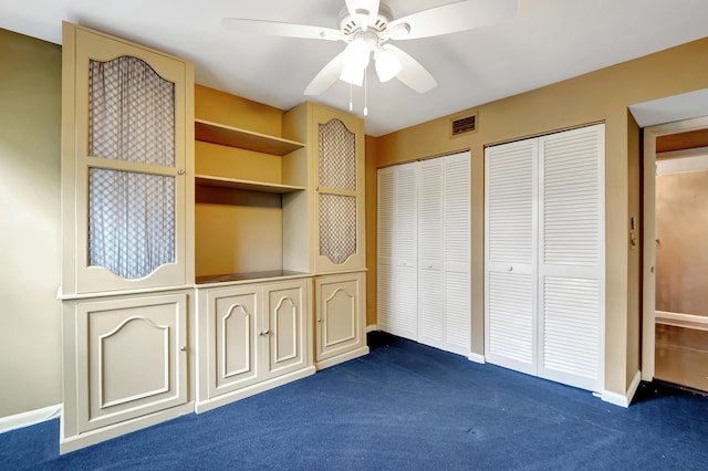 unfurnished bedroom with two closets, ceiling fan, and dark colored carpet