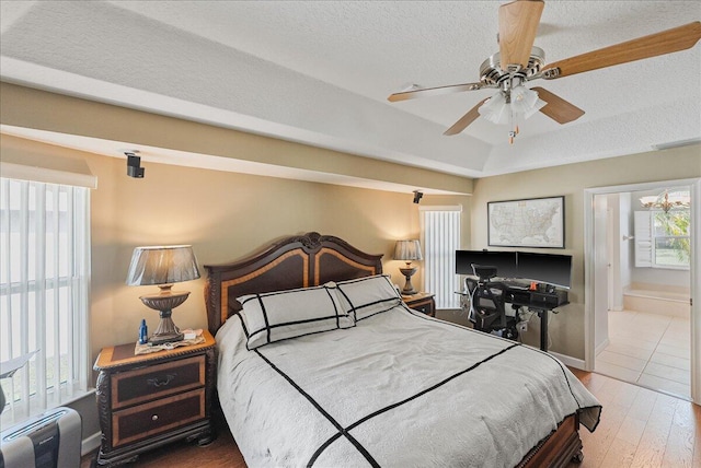 bedroom with ensuite bath, ceiling fan, light hardwood / wood-style floors, and a textured ceiling