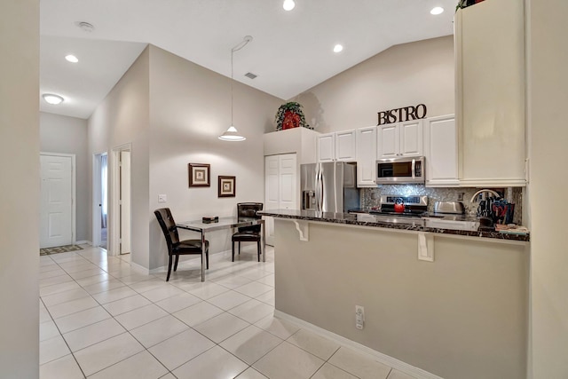 kitchen with high vaulted ceiling, hanging light fixtures, light tile patterned floors, dark stone countertops, and stainless steel appliances