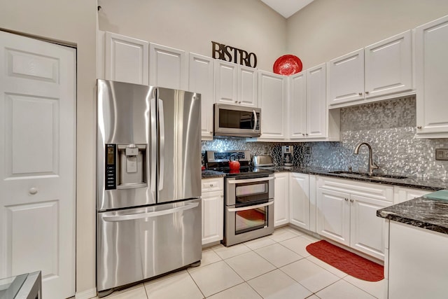 kitchen featuring sink, light tile patterned floors, appliances with stainless steel finishes, white cabinetry, and dark stone counters