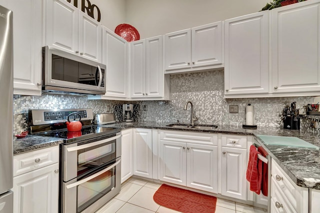 kitchen with light tile patterned flooring, appliances with stainless steel finishes, white cabinetry, sink, and backsplash