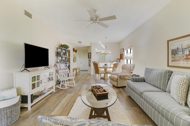 living room featuring ceiling fan with notable chandelier, light wood-type flooring, and a textured ceiling