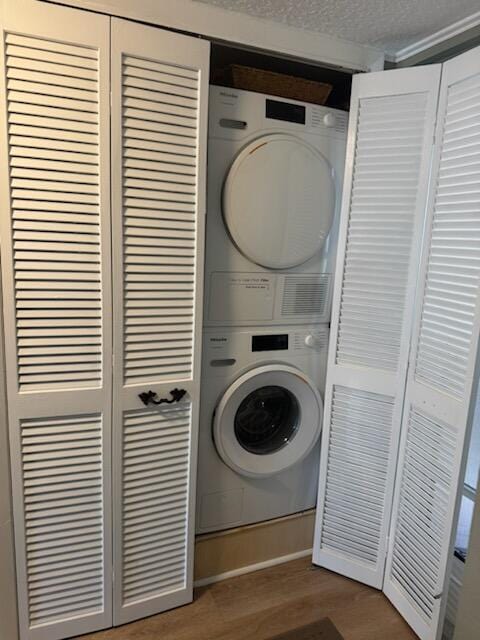 clothes washing area with a textured ceiling, wood-type flooring, and stacked washer and dryer