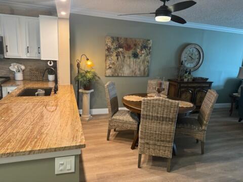 dining space with ceiling fan, sink, light hardwood / wood-style floors, and ornamental molding